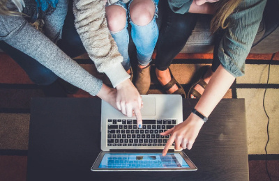 three people sat on a sofa pointing to an open laptop screen on a table